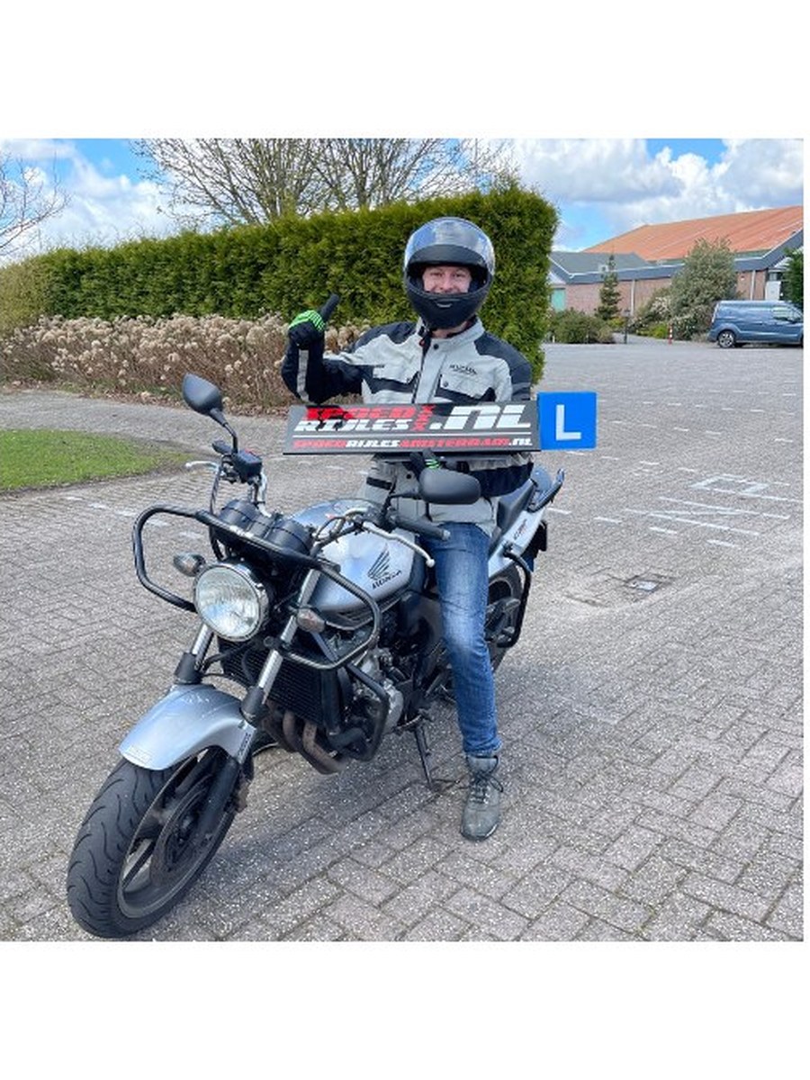 Geslaagde motorleerling naast de lesmotor met het SPOEDRIJLES-bord